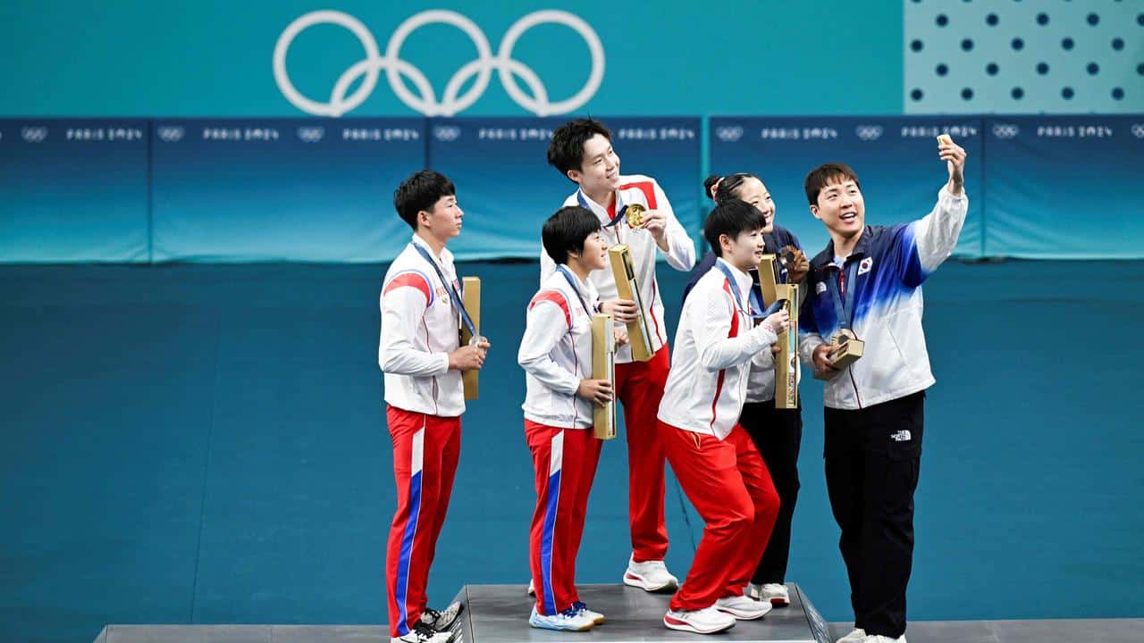 Bronze medalists South Korea's Lim Jonghoon (R) takes a selfie picture with his mobile as he celebrates on the podium with : gold medalists China's Wang Chuqin (rear 2nd L) and China's Sun Yingsha (front 2nd L), silver medalists North Korea's Ri Jong Sik (L), and North Korea's Kim Kum Yong (front 2nd L) and bronze medallist and teammate South Korea's Shin Yubin (2nd R) at the end of their mixed table tennis doubles competition at the Paris 2024 Olympic Games at the South Paris Arena in Paris on July 30, 2024. (Photo by WANG Zhao / AFP)