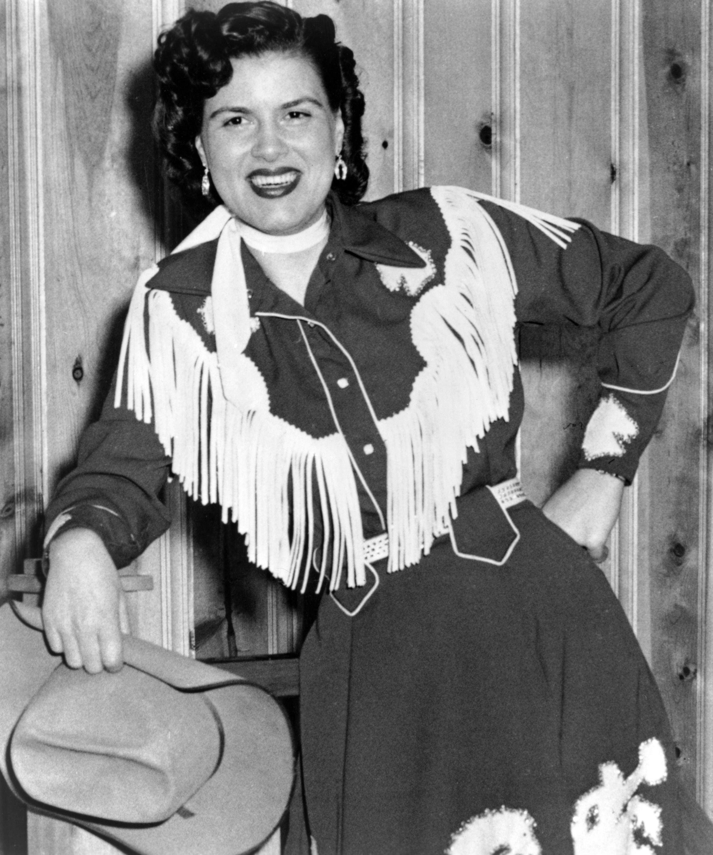 Country musician Patsy Cline wearing a fringed dress and holding a cowboy hat in circa 1958. 